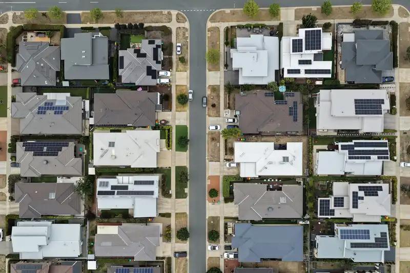 Aerial view of a suburban street where several houses have solar panels on their roofs