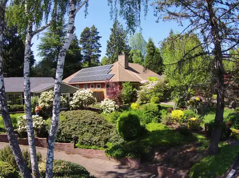 A house roof with a rooftop solar panel array seen through trees